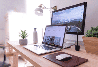 A laptop on a desk along with a mouse, an external monitor, and a desk lamp.